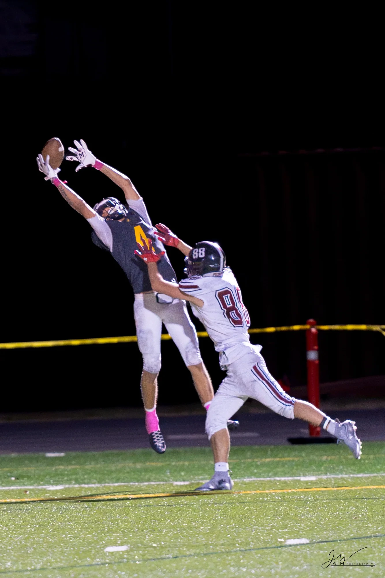 Two football players leap toward a pass against the dark night sky